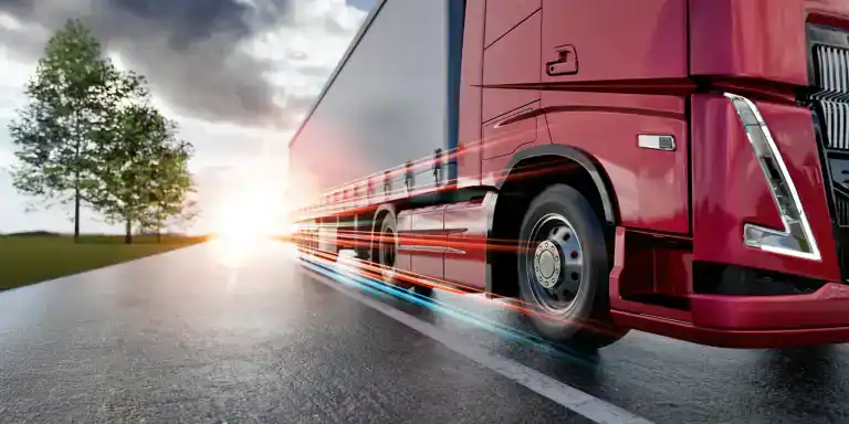 A red semi-truck speeds down a wet CA road at sunrise or sunset, with motion blur effects emphasizing its movement. Trees and a dramatic sky frame the scene, highlighting the Clean Truck Check in Los Angeles & Riverside County.